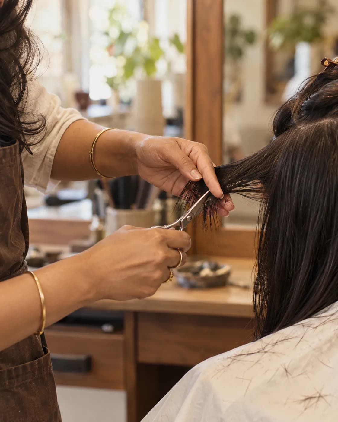 Close-up of a hairstylist's hands holding a section of a client's dark hair and trimming it with a pair of scissors.